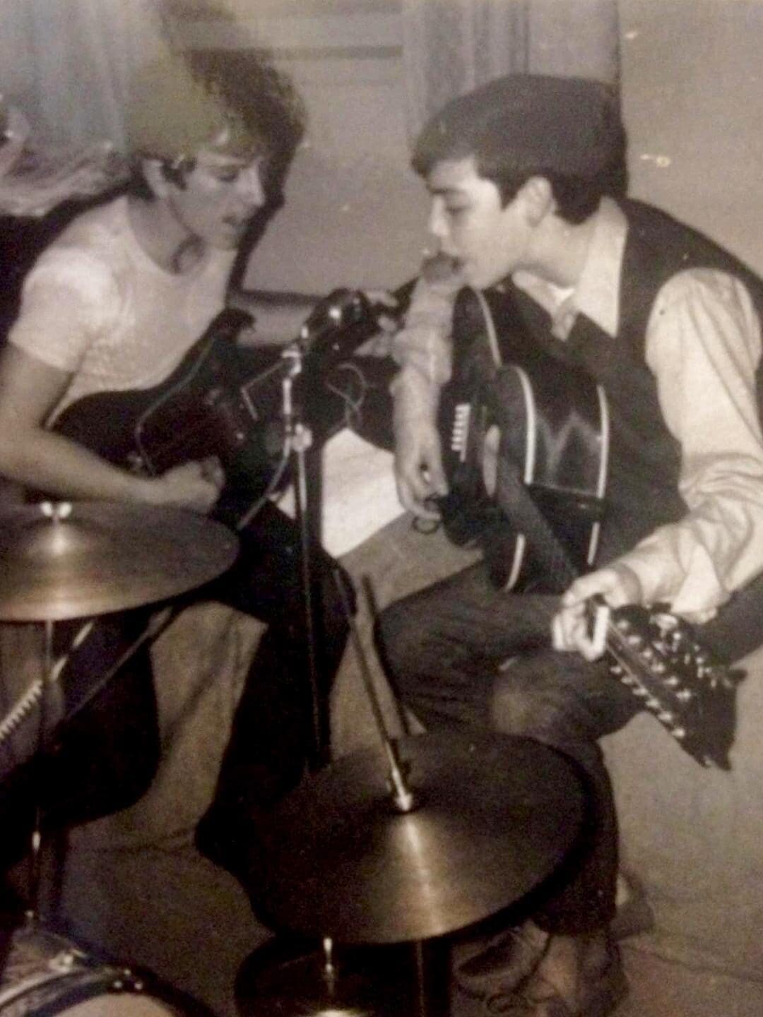 Two young men playing drums and guitar in a room.